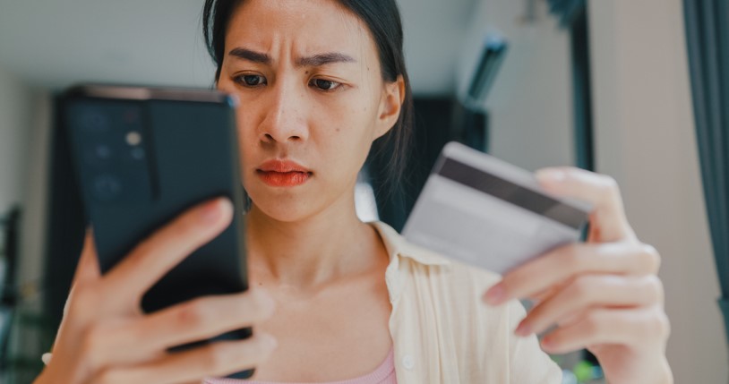Woman looking at phone and credit card with concern
