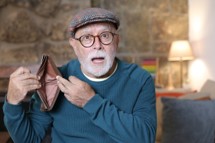 Older man with a look of surprise holding up an empty wallet