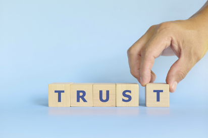 Hand putting letter blocks together to spell 'trust'