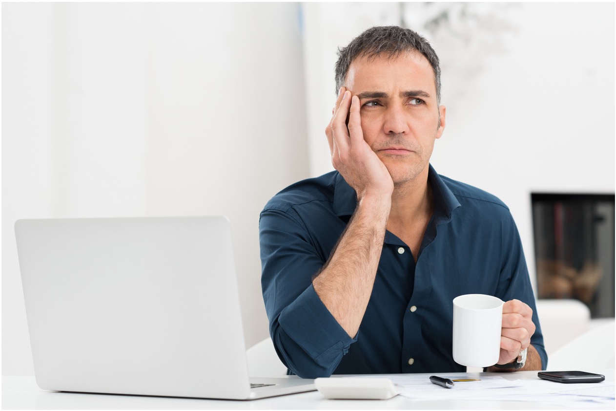 Man sits in front of laptop drinking coffee and looking forlorn