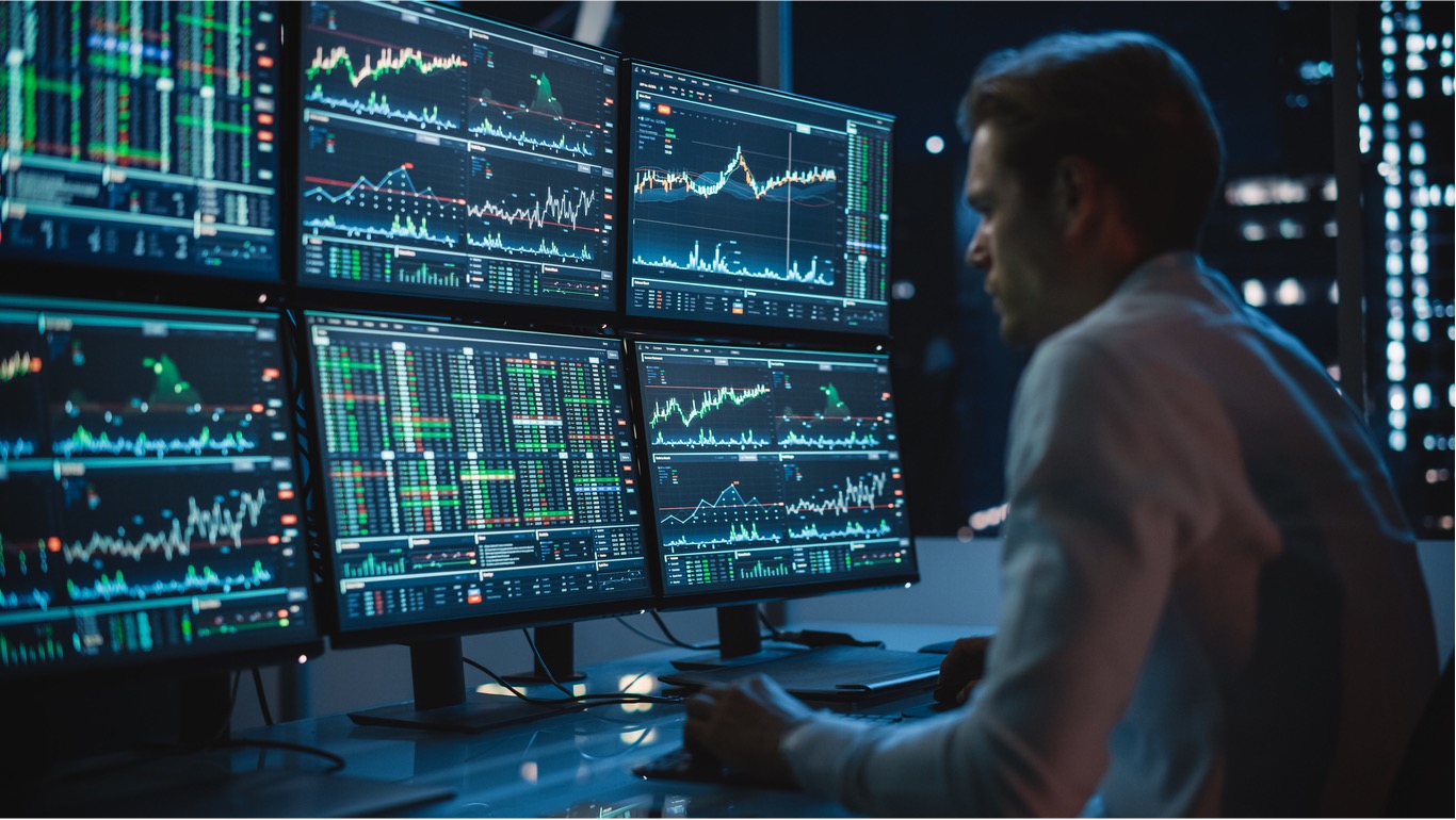 Man sits in front of six monitors displaying graphs