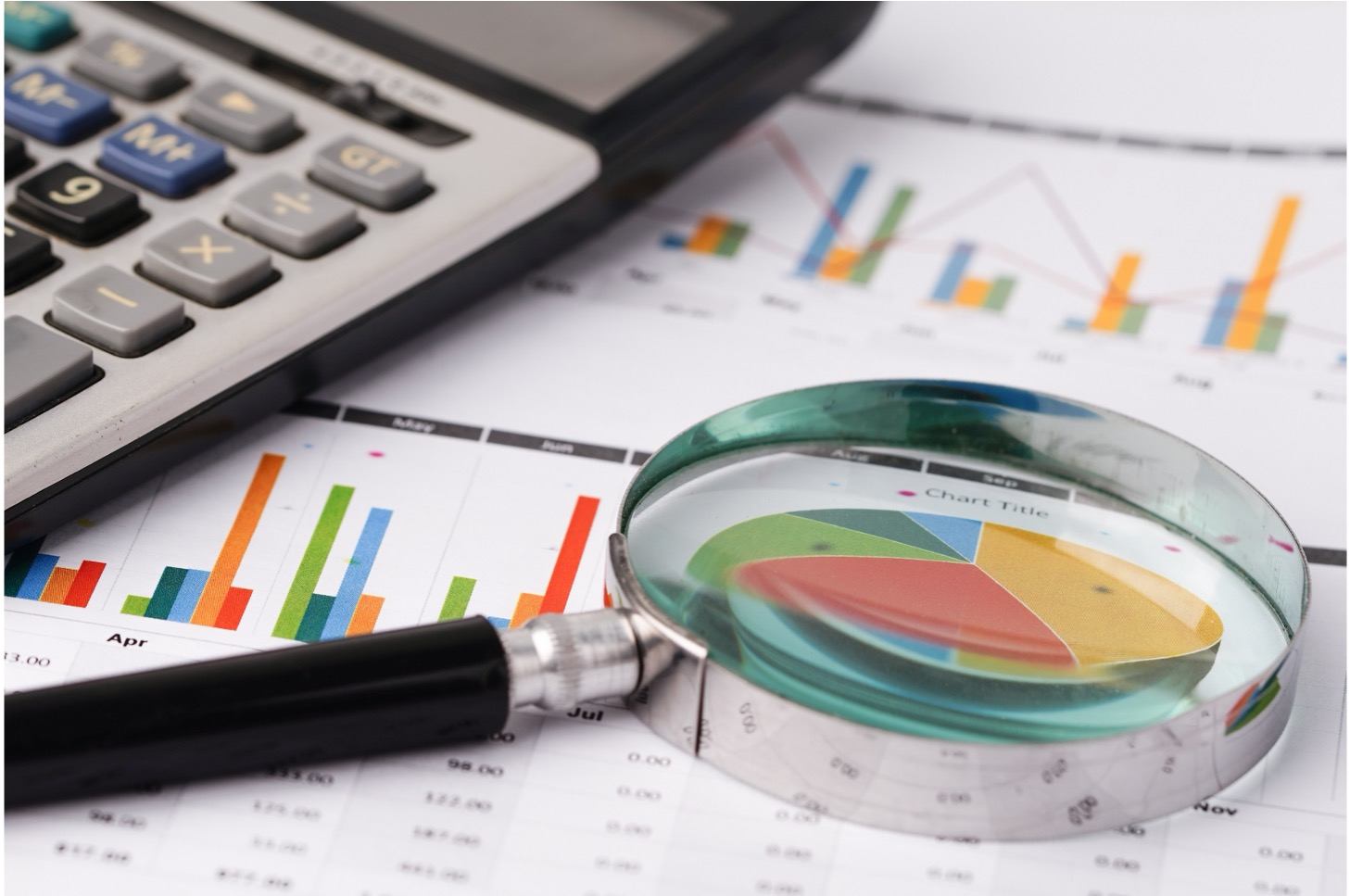 Image of a magnifying glass and a calculator on top of a paper full of graphs