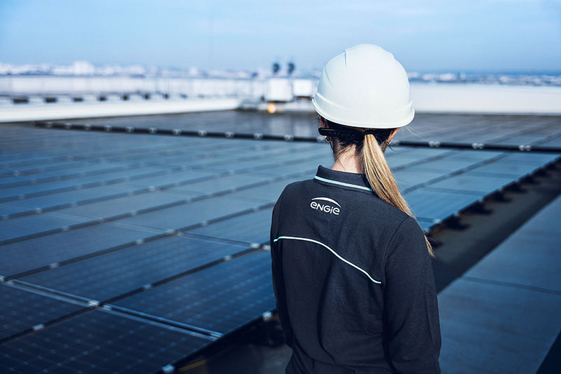 A woman with hard hat and Engie shirt on looking at solar panels