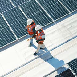 Two men walking in hard hats near a solar panel